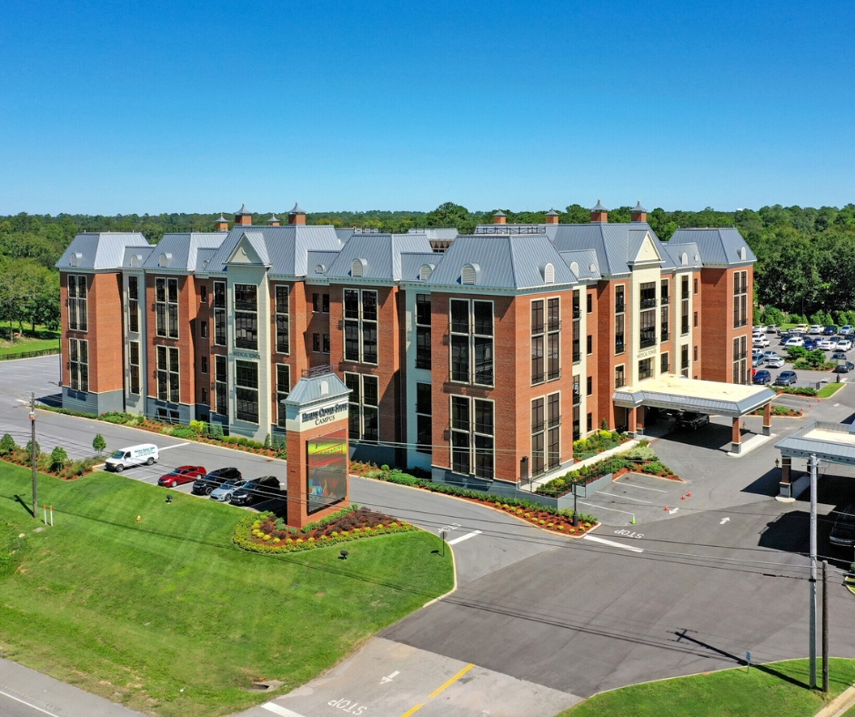A drone image of a large buidling with forest in the background and blue sky